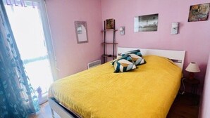 Una camera da letto con un letto, cuscini, un comodino, una lampada e una finestra con tende.