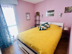 Ein Schlafzimmer mit einem Bett, Kissen, einem Nachttisch, einer Lampe und einem Fenster mit Vorhängen.