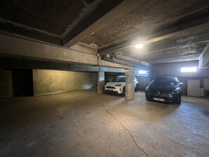 Eine mehrstöckige Tiefgarage mit Betonböden und -wänden, zwei geparkte Autos und eine einzelne Deckenleuchte.