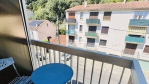 Un balcone con un tavolo blu e sedie bianche, con vista su una zona residenziale con edifici e cielo sereno.