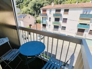 Ein Balkon mit einem blauen Tisch und weißen Stühlen, der auf ein Wohngebiet mit Gebäuden und einem klaren Himmel blickt.