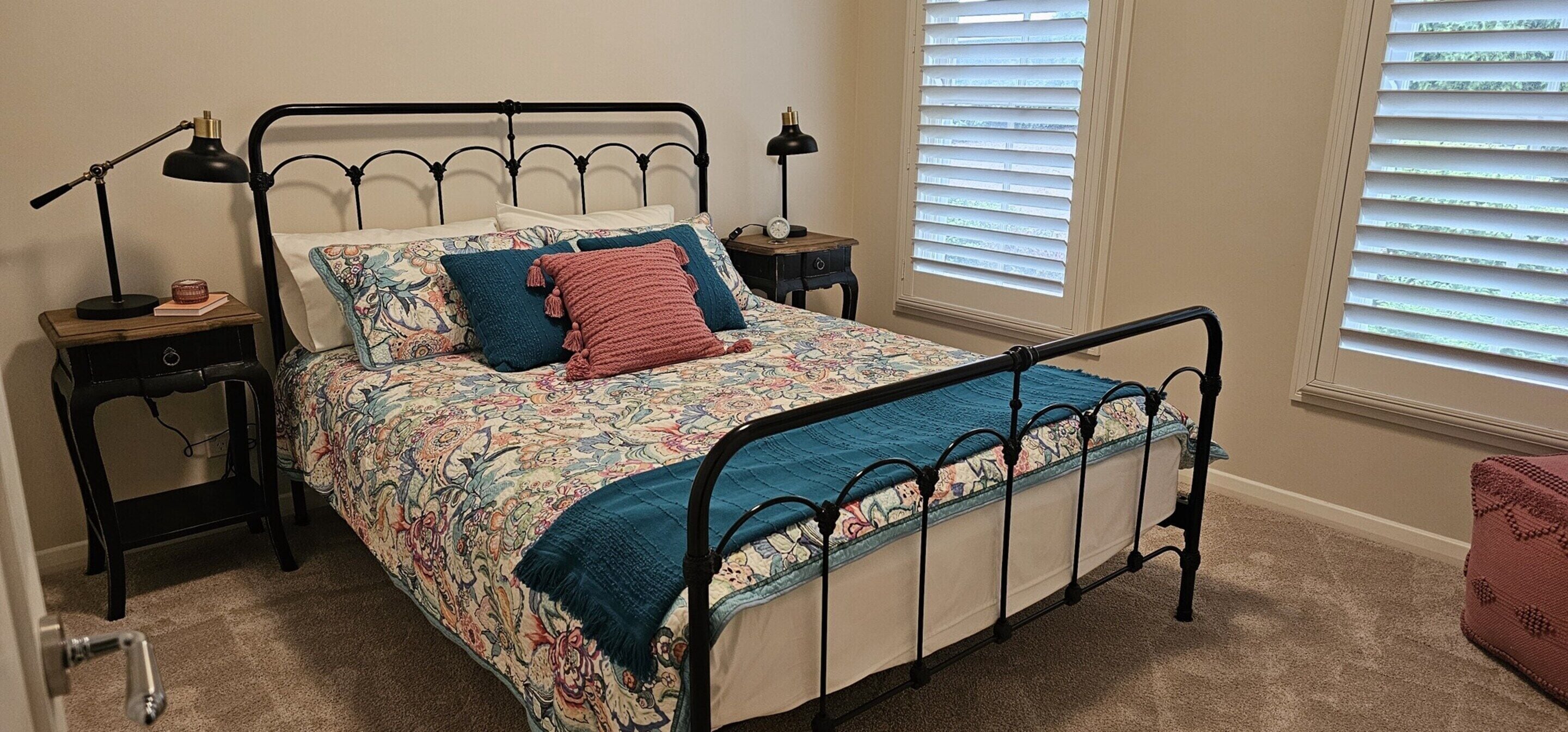 A bed with a floral bedspread, two pillows, a blue blanket, and a metal frame. There are two bedside tables with lamps and a clock.