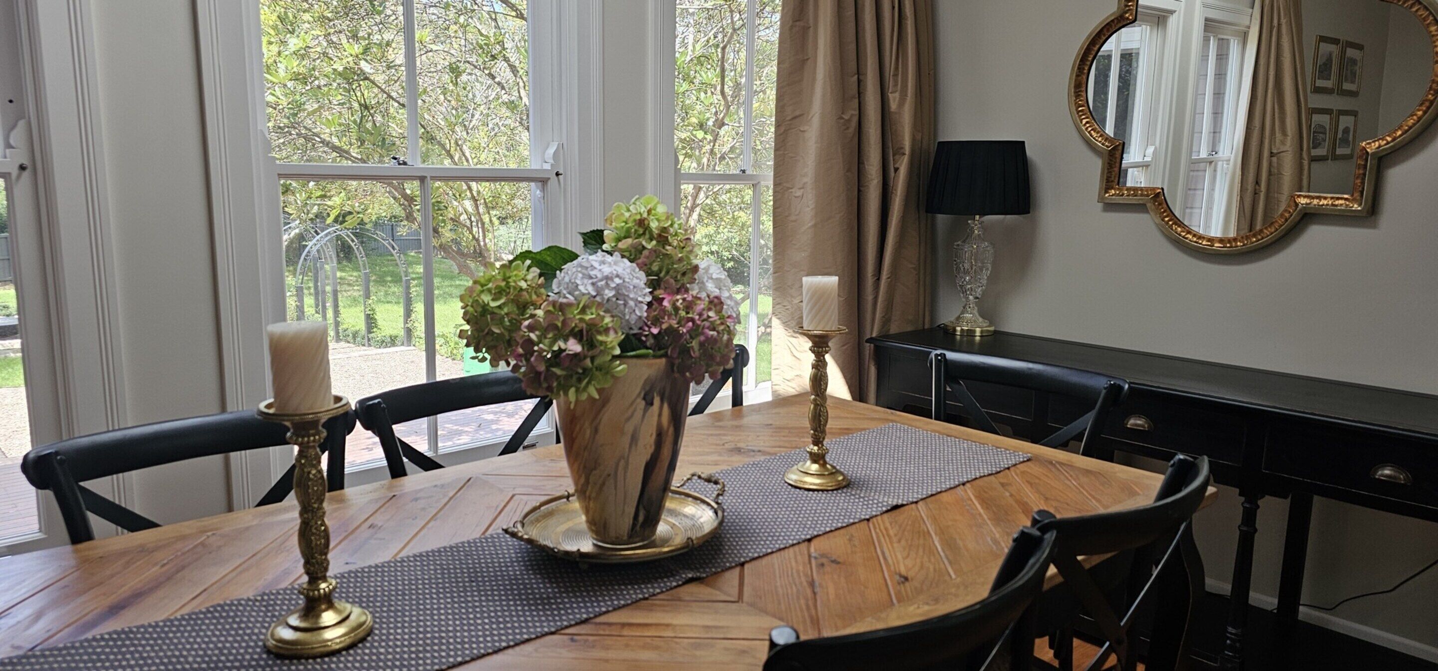 A dining table with a vase of flowers, candles, and a mirror on the wall.