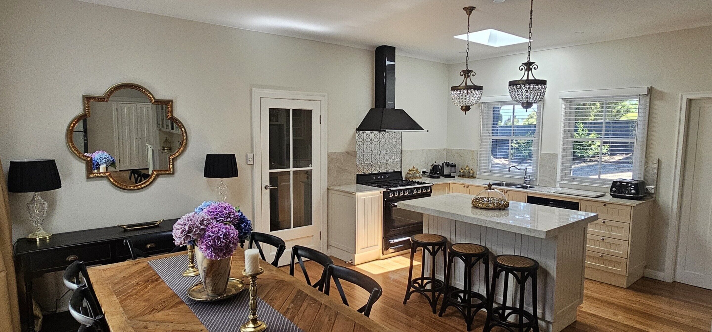 A modern kitchen with a central island, a dining table with chairs, and a large mirror on the wall.