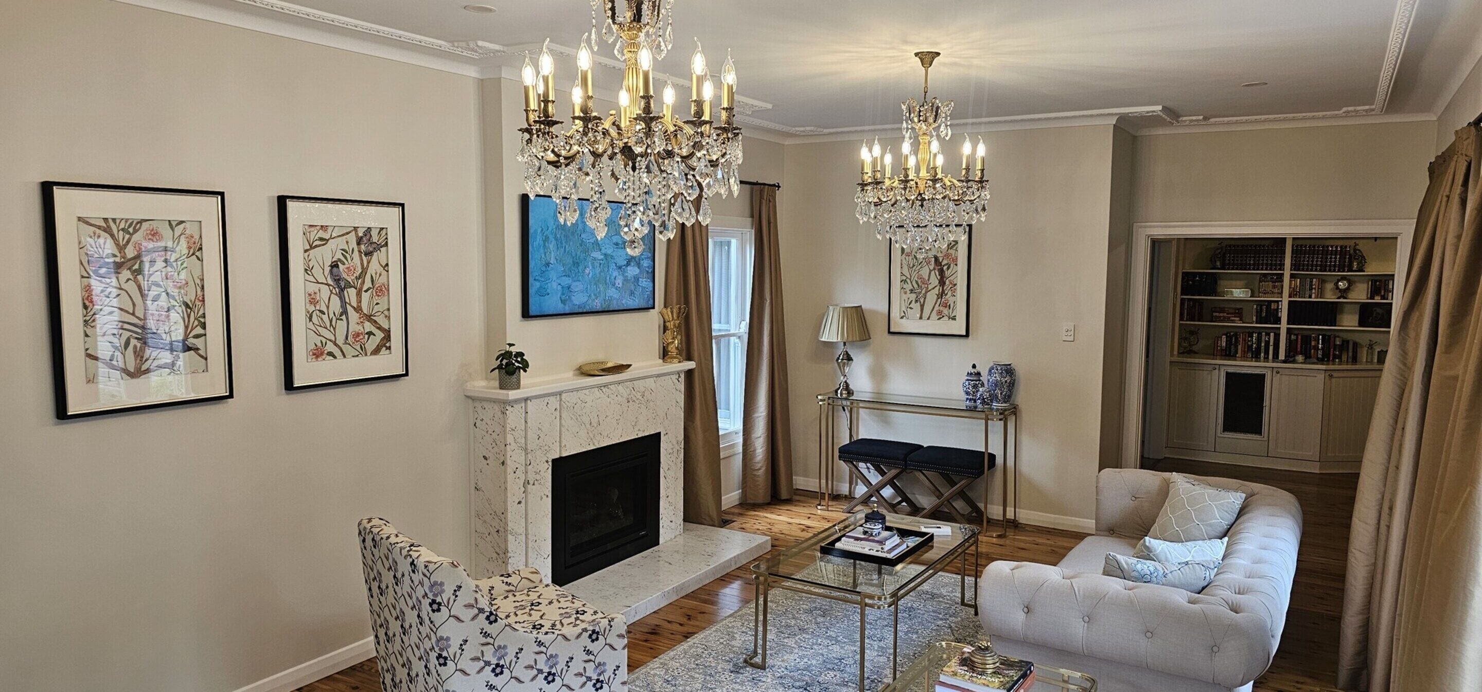 A living room with a fireplace, a chandelier, a sofa, and a bookshelf.