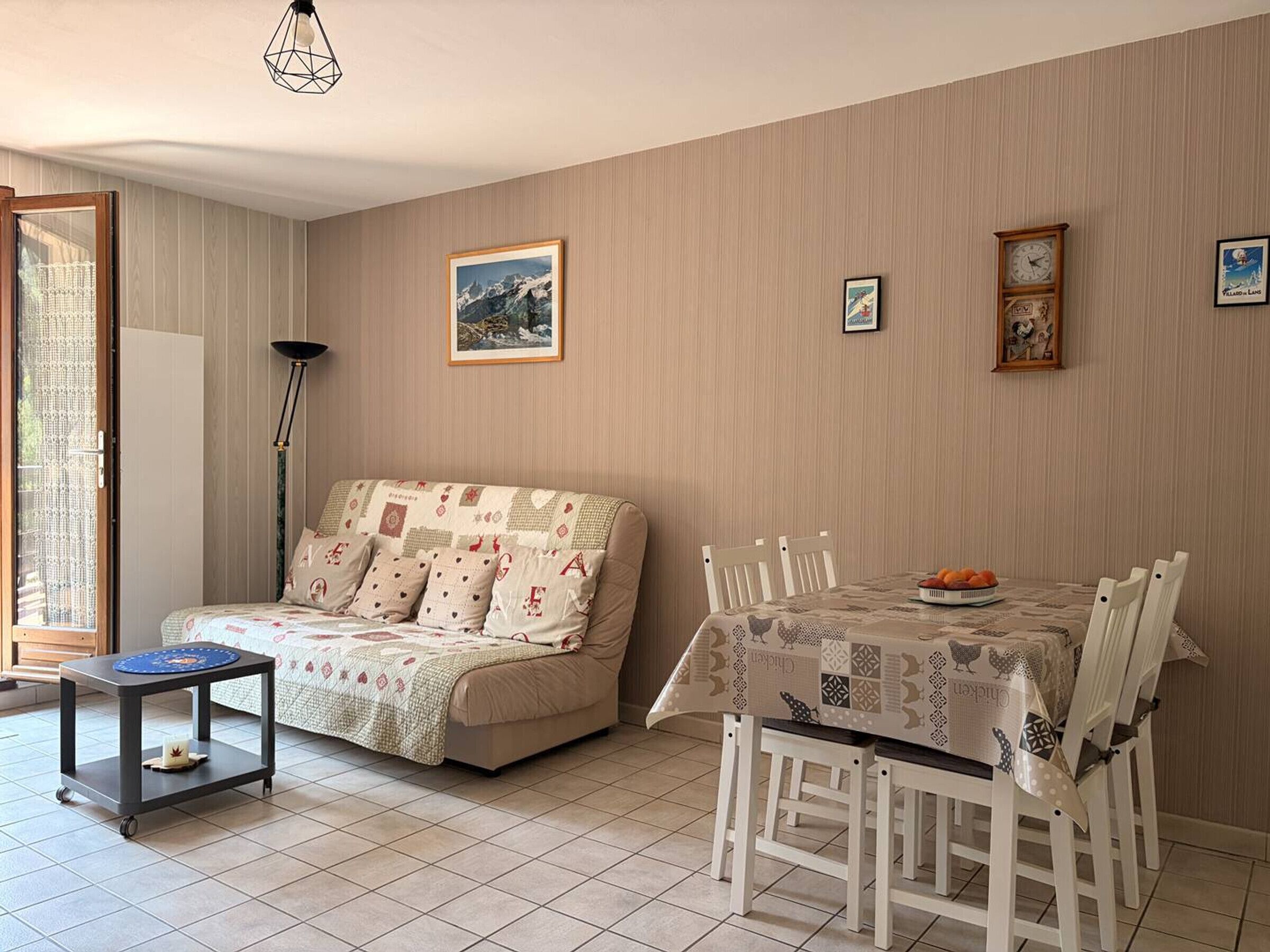 A cozy living room with a sofa, a dining table with chairs, a side table, and a floor lamp.