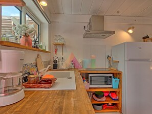 Eine kleine Küche mit einer Mikrowelle, einem Kühlschrank und einem Waschbecken. Regale mit Einmachgläsern und ein Fenster, das für natürliches Licht sorgt.