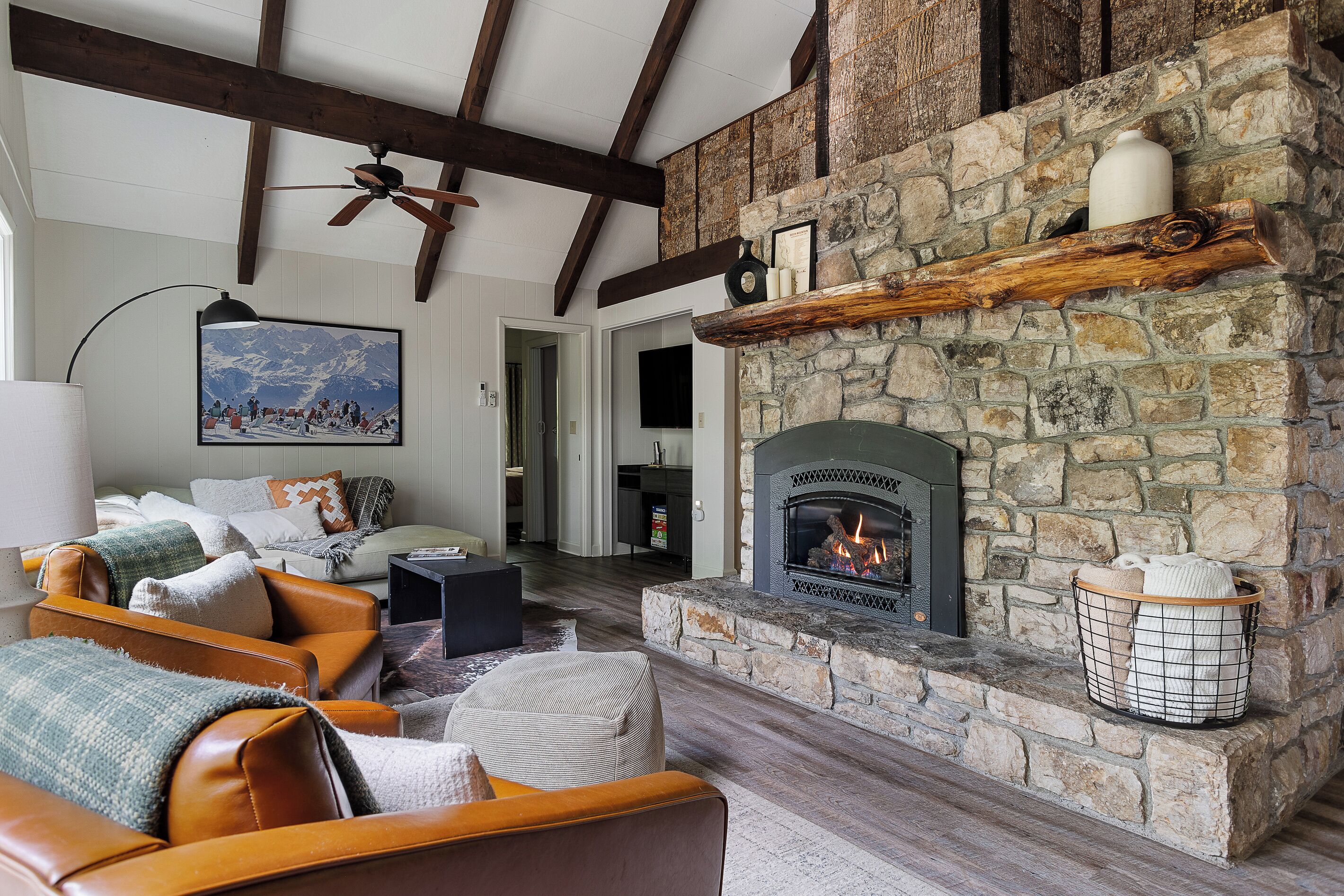 A cozy living room with a stone fireplace, leather sofas, and a painting of a snowy mountain scene.