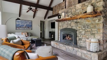A cozy living room with a stone fireplace, leather sofas, and a painting of a snowy mountain scene.