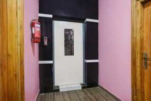 A hallway with a white door, a fire extinguisher on the wall, and a wooden door on the right.