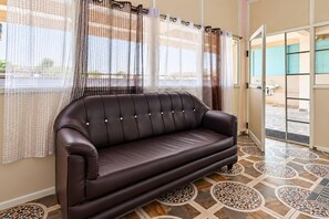 A brown leather sofa in a room with patterned floor tiles and sheer curtains with a brown and white pattern. - Hotel O Achampeta Junction Kakinada (Kakinada)
