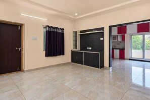 Ein geräumiger Raum mit einer dunkelholzigen Tür, einem Fenster mit violetten Vorhängen, einem schwarzen Schrank und einer strukturierten Wand darüber sowie einem roten und weißen Schrank mit Glastür.