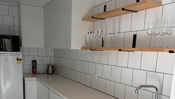 Een moderne keuken met witte kasten, een roestvrijstalen spoelbak en een houten plank boven het aanrecht.