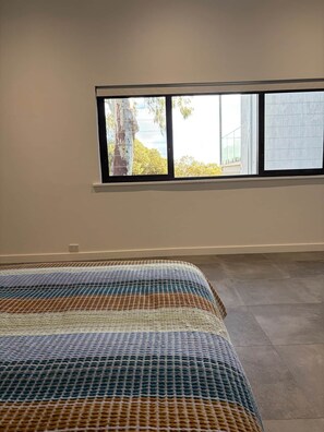 A room with a large window, a bed with a patterned bedspread, and a tiled floor.