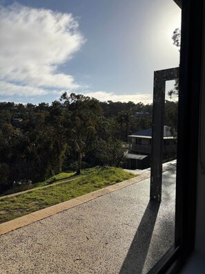 Une vue à travers une fenêtre, avec un ciel dégagé, une route et un immeuble doté d’un balcon.