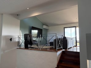 A modern interior with a staircase leading to a balcony, a seating area with a sofa and armchairs, and a large window providing natural light. - Perth Hills Retreat | City Views | Luxury Beds (Gooseberry Hill)