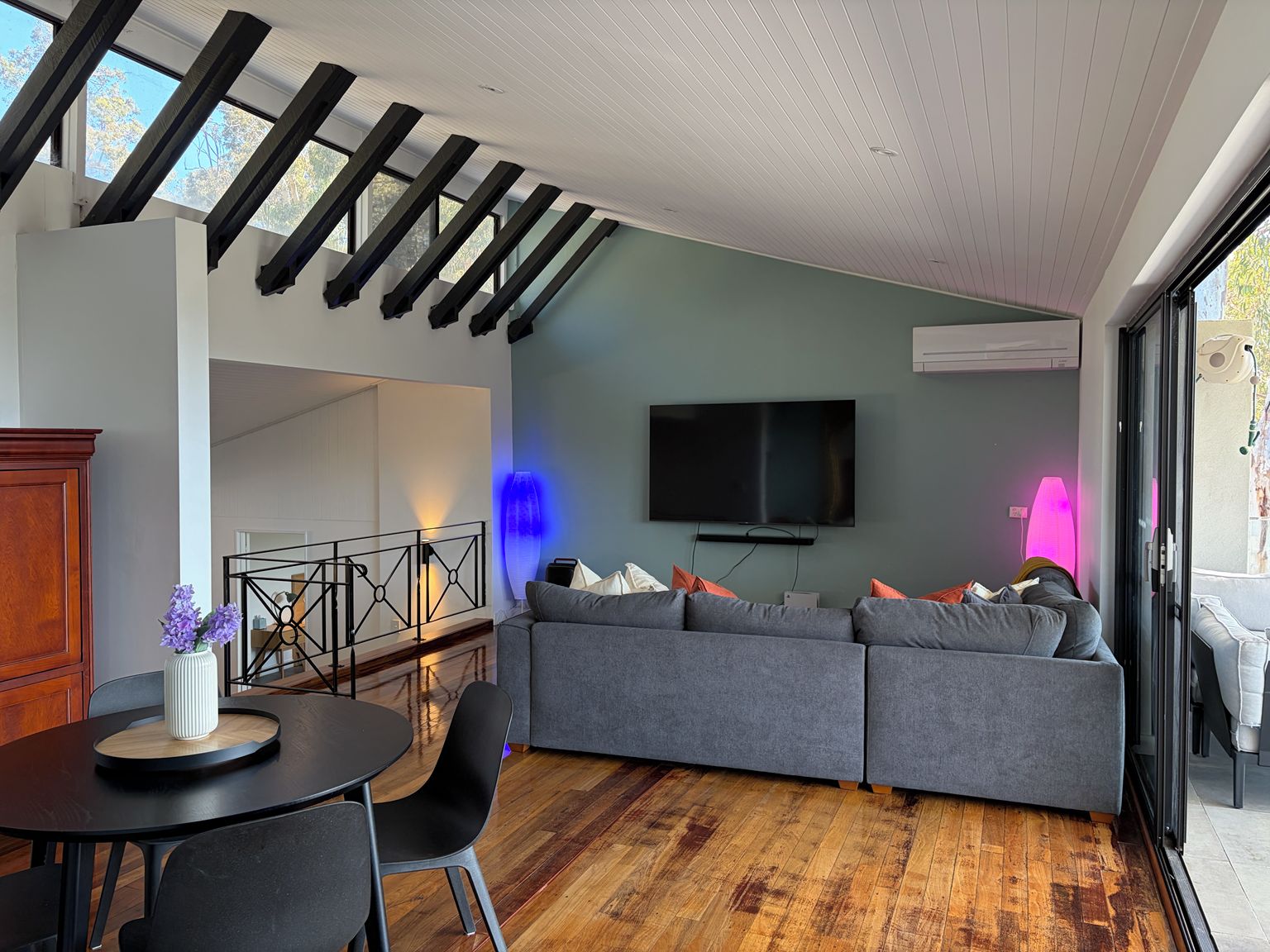 A modern living room with a sectional sofa, a flat-screen TV, and a dining area with a round table and chairs.
