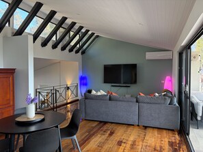 Een moderne woonkamer met een hoekbank, een flatscreen televisie en een eetgedeelte met een ronde tafel en stoelen.