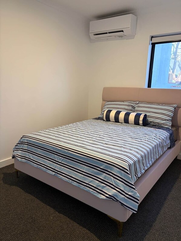 A bedroom with a bed, a window, and an air conditioning unit.