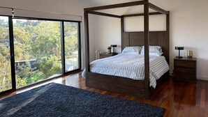 A bedroom with a four-poster bed, a large window, and a ceiling fan.