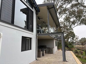 A two-story house with a covered outdoor area, a grill, and a pergola.