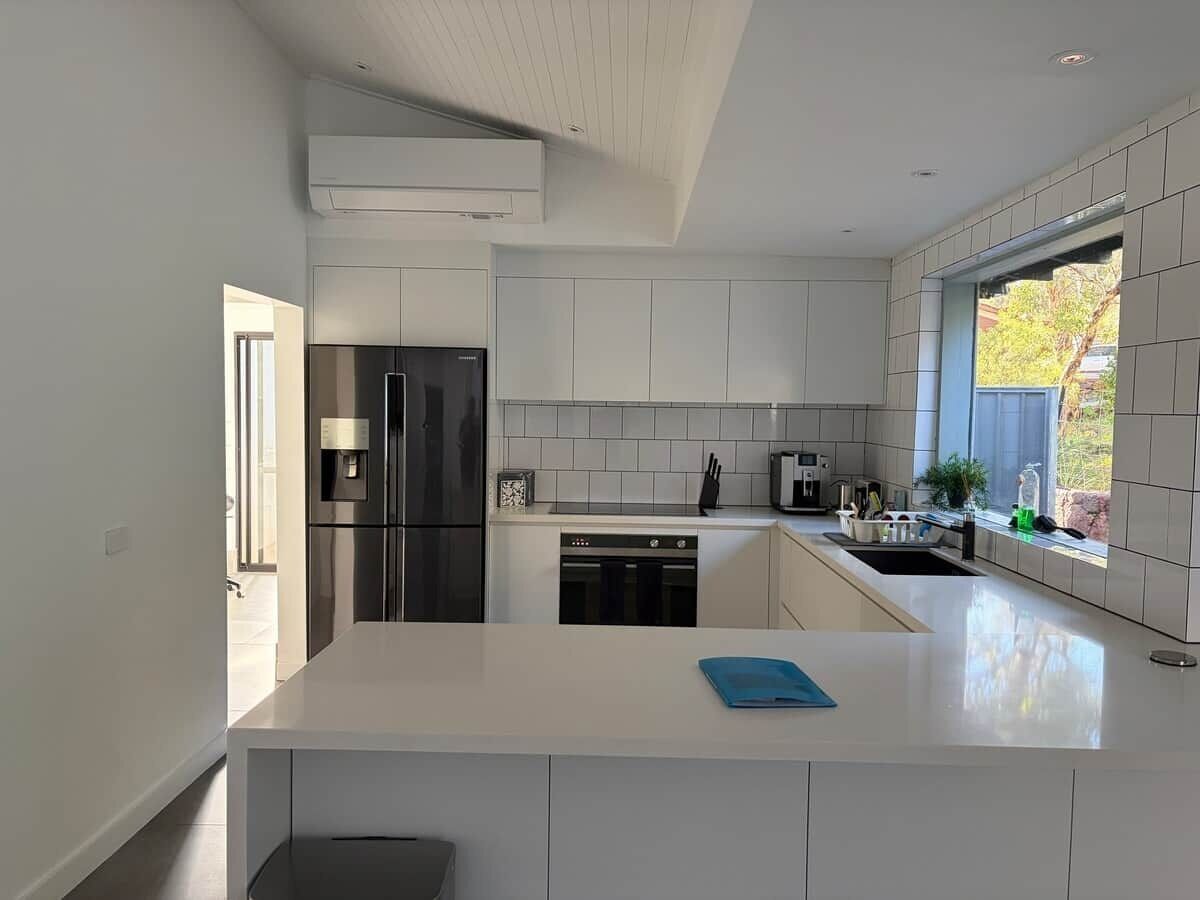 A modern kitchen with white cabinetry, a stainless steel refrigerator, a dishwasher, and a window providing natural light.