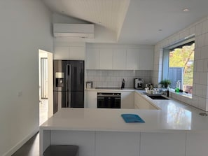 A modern kitchen with white cabinetry, a stainless steel refrigerator, a dishwasher, and a window providing natural light.