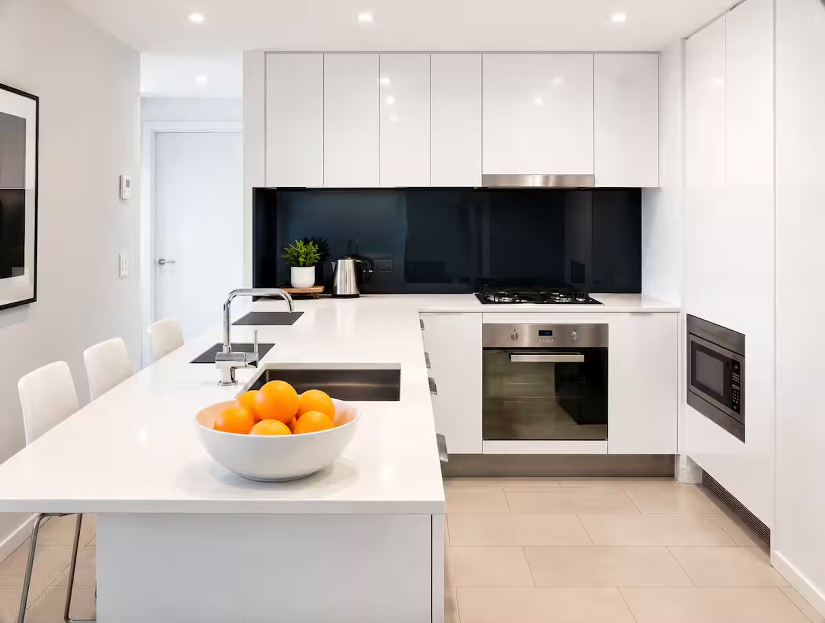 A modern kitchen with white cabinetry, a central island with a bowl of fruit, and built-in appliances.