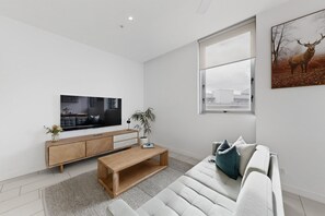 A modern living room with a flat-screen TV, wooden furniture, a large window, and a framed picture of a deer. - City View 2-bed Apartment Fortitude Valley (Brisbane)