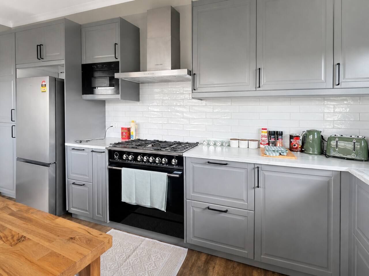 A modern kitchen with grey cabinets, a stainless steel refrigerator, a gas stove, and a white countertop.