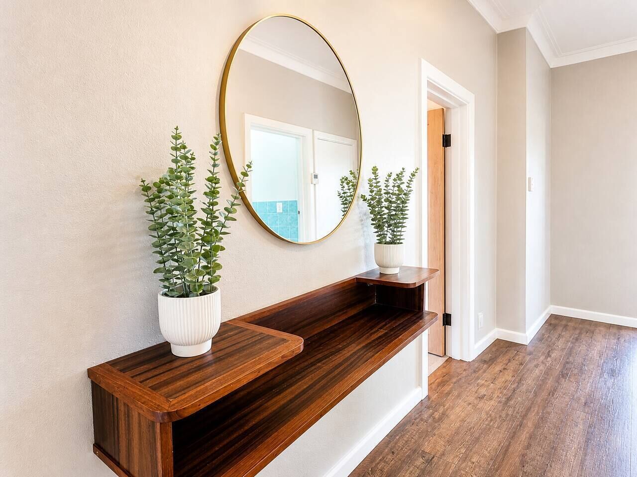 A hallway with a wooden bench, a round mirror, and two potted plants.