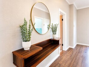 A hallway with a wooden bench, a round mirror, and two potted plants. - "Premium 3BR Mt View • Sleeps 8 • 15 min Canberra" (Queanbeyan)