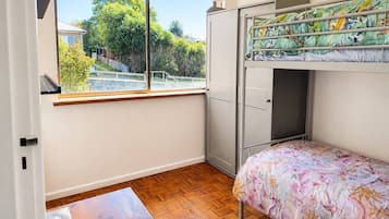 Une chambre avec un lit superposé, une petite table, une fenêtre donnant sur un espace verdoyant et une porte.