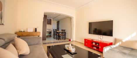 Una sala moderna con un sofá, una mesa de centro, un televisor y un área de comedor al fondo.