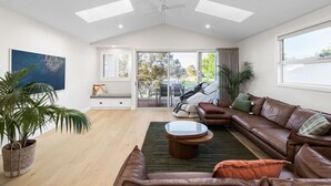 Uma sala de estar ampla com um sofá de couro marrom, uma mesa de centro e um vaso com planta.