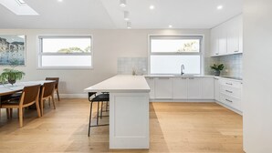 Uma cozinha moderna com armários brancos, uma ilha central e um espaço de jantar com cadeiras de madeira e uma mesa.