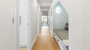 Um corredor estreito com uma cama no final, piso de madeira e paredes brancas.