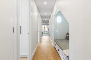 A narrow hallway with a bed at the end, wooden flooring, and white walls. - Oakwood Retreat in Rosebud (Melbourne)