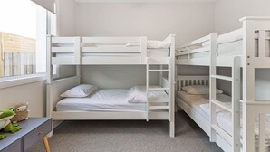 Quarto com beliche, roupa de cama branca, escrivaninha e janela.