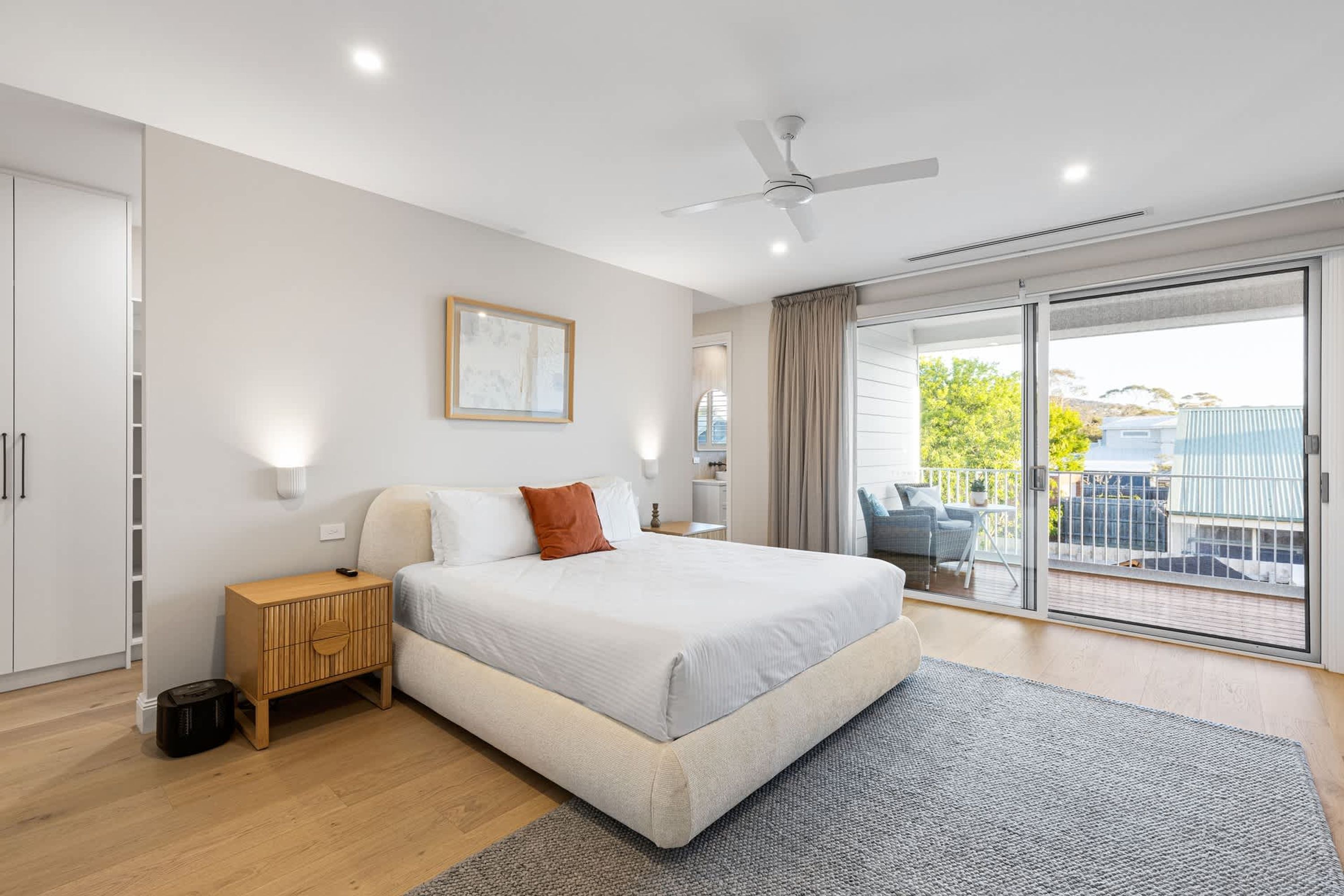 A modern bedroom with a large bed, a ceiling fan, a view to the outside, and a sliding glass door.