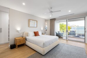 Quarto moderno com uma cama grande, um ventilador de teto, vista para o exterior e uma porta de vidro deslizante.