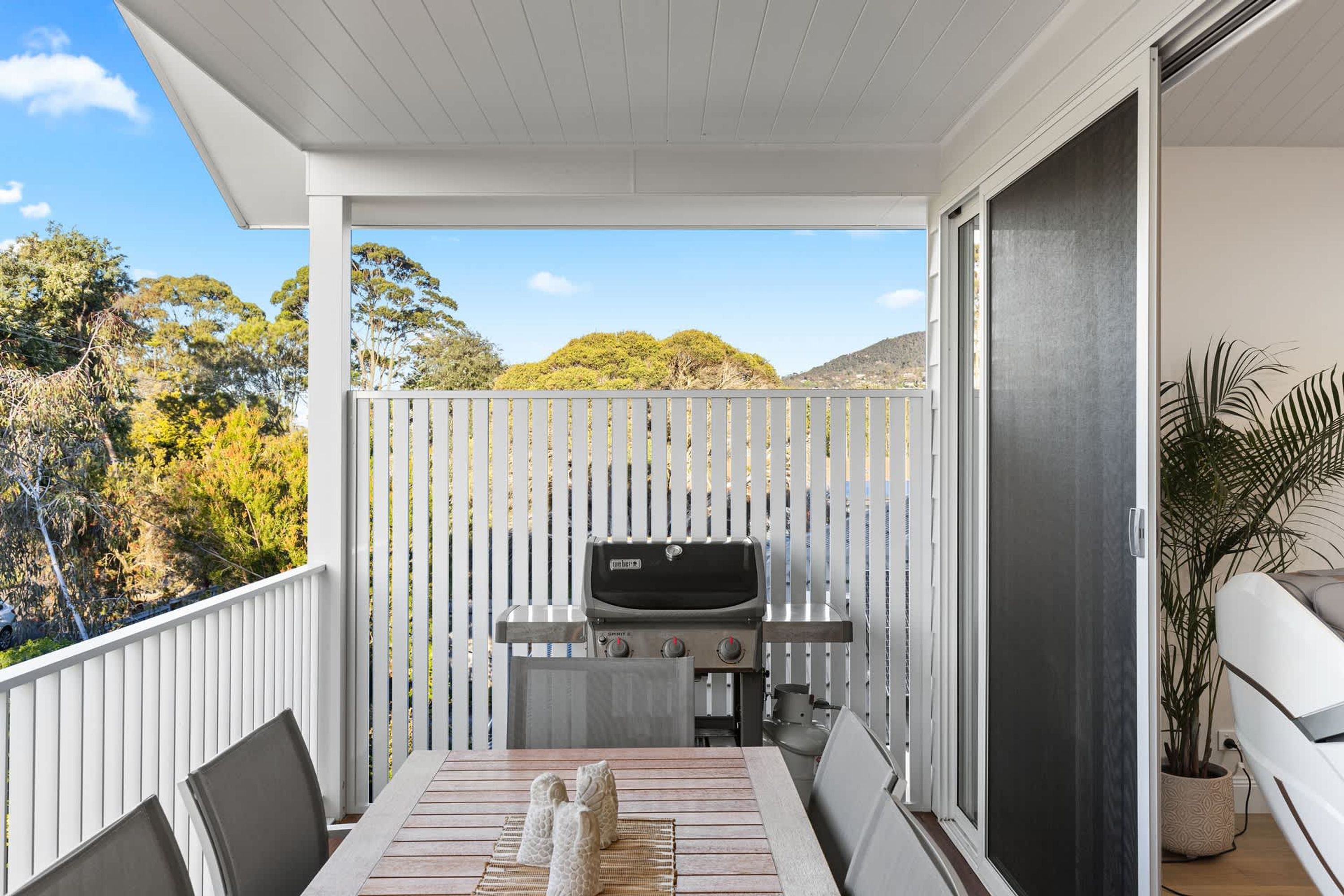A balcony with a barbecue grill, a dining table with chairs, and a potted plant.