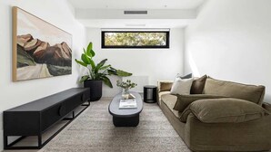 Ein modernes Wohnzimmer mit einer Couch, einem Couchtisch, einer Kommode, einer Topfpflanze und einem gerahmten Bild an der Wand.