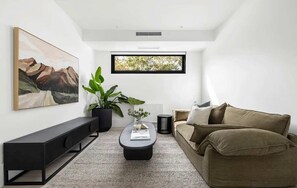 Ein modernes Wohnzimmer mit einer Couch, einem Couchtisch, einer Kommode, einer Topfpflanze und einem gerahmten Bild an der Wand.