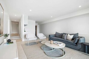 A modern living room with a grey sofa, two white chairs, a coffee table, and a small side table with a plant. - El v Luxury in Mount Martha With Gas Heated Pool Bay Views (Melbourne)
