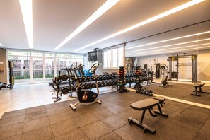 Ein modernes Fitnessstudio mit verschiedenen Trainingsgeräten, großen Fenstern und Blick auf Grünflächen.