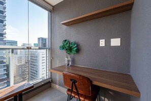 A modern interior with a wooden desk, a chair, a potted plant, and a view of the city through a large window. - Mc601-1810 You Faria Lima (São Paulo)