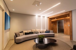 A modern lounge area with a curved sofa, a round coffee table, and a wooden accent wall. - Mc601-1810 You Faria Lima (São Paulo)