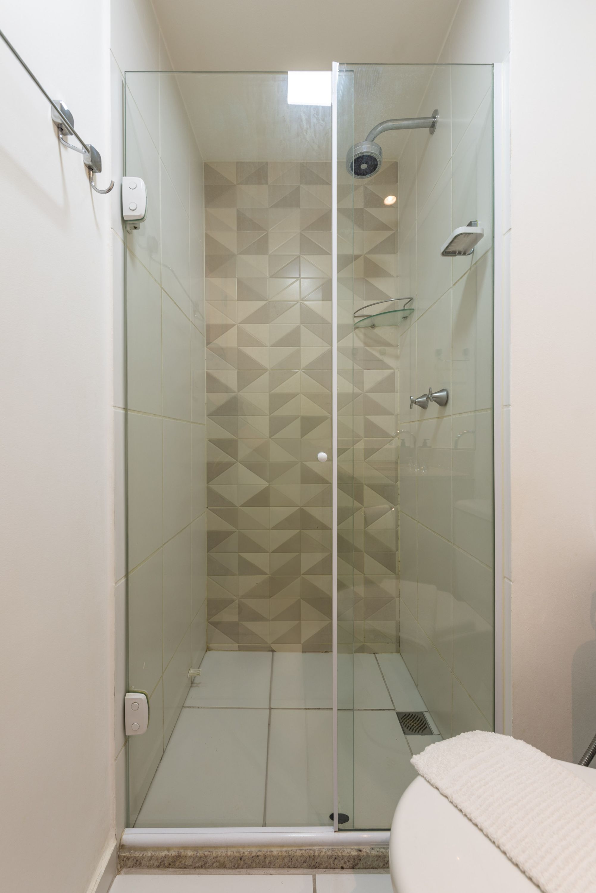 A glass-enclosed shower stall with a geometric tile pattern on the walls.