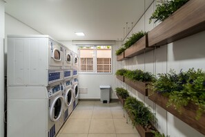 A laundry room with stacked washing machines, a window with a view, and wooden shelves with plants. - Mc601-1810 You Faria Lima (São Paulo)